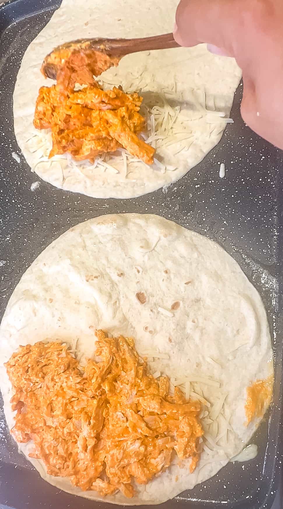 Close up shot of buffalo chicken mixture on half of a tortilla.