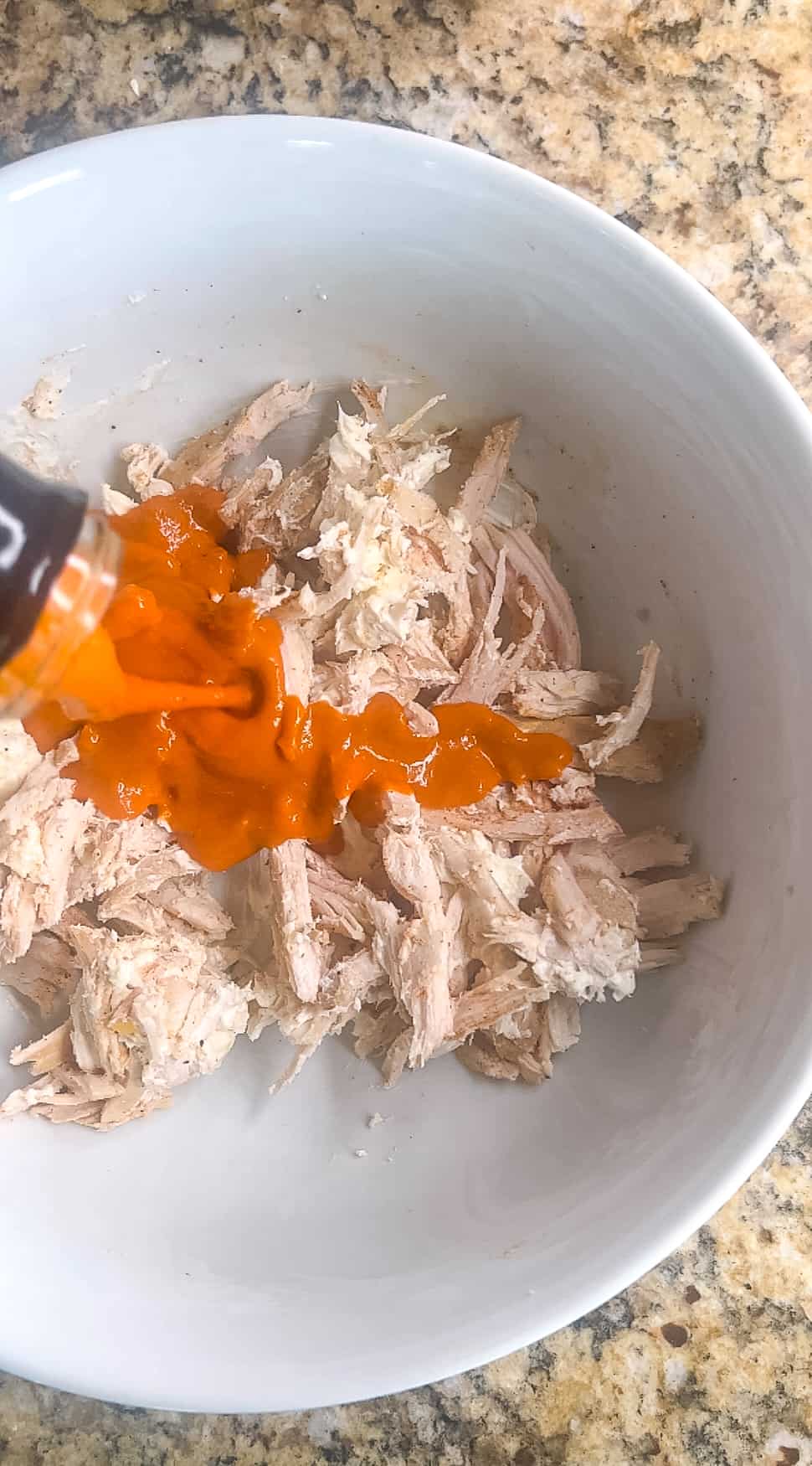 Buffalo sauce being added to shredded chicken and cream cheese mixture.