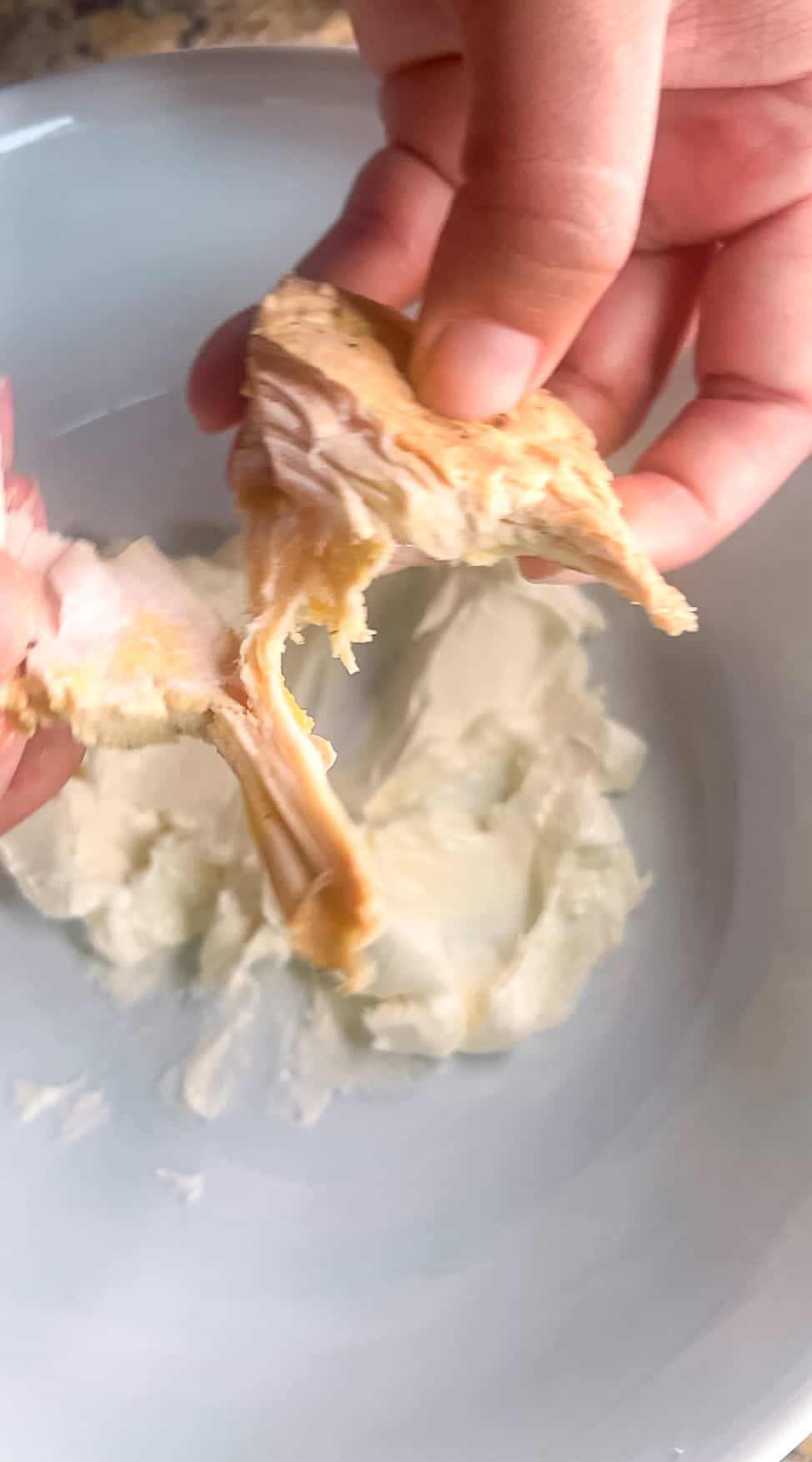 Hands shredding chicken over a bowl of cream cheese.