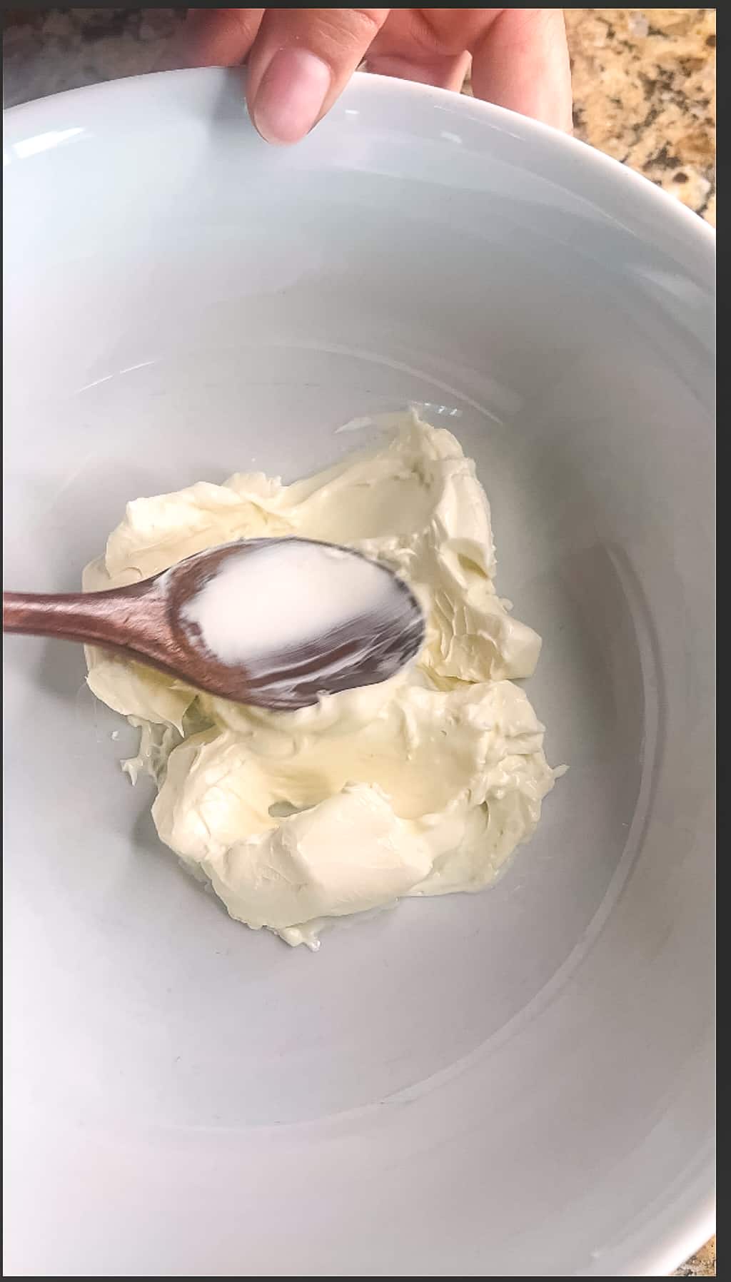 A bowl of softened cream cheese with a spoon in the center.