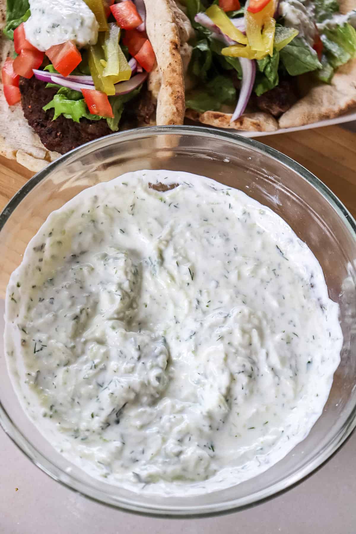tzatziki sauce in a bowl with gyro sandwiches in the background