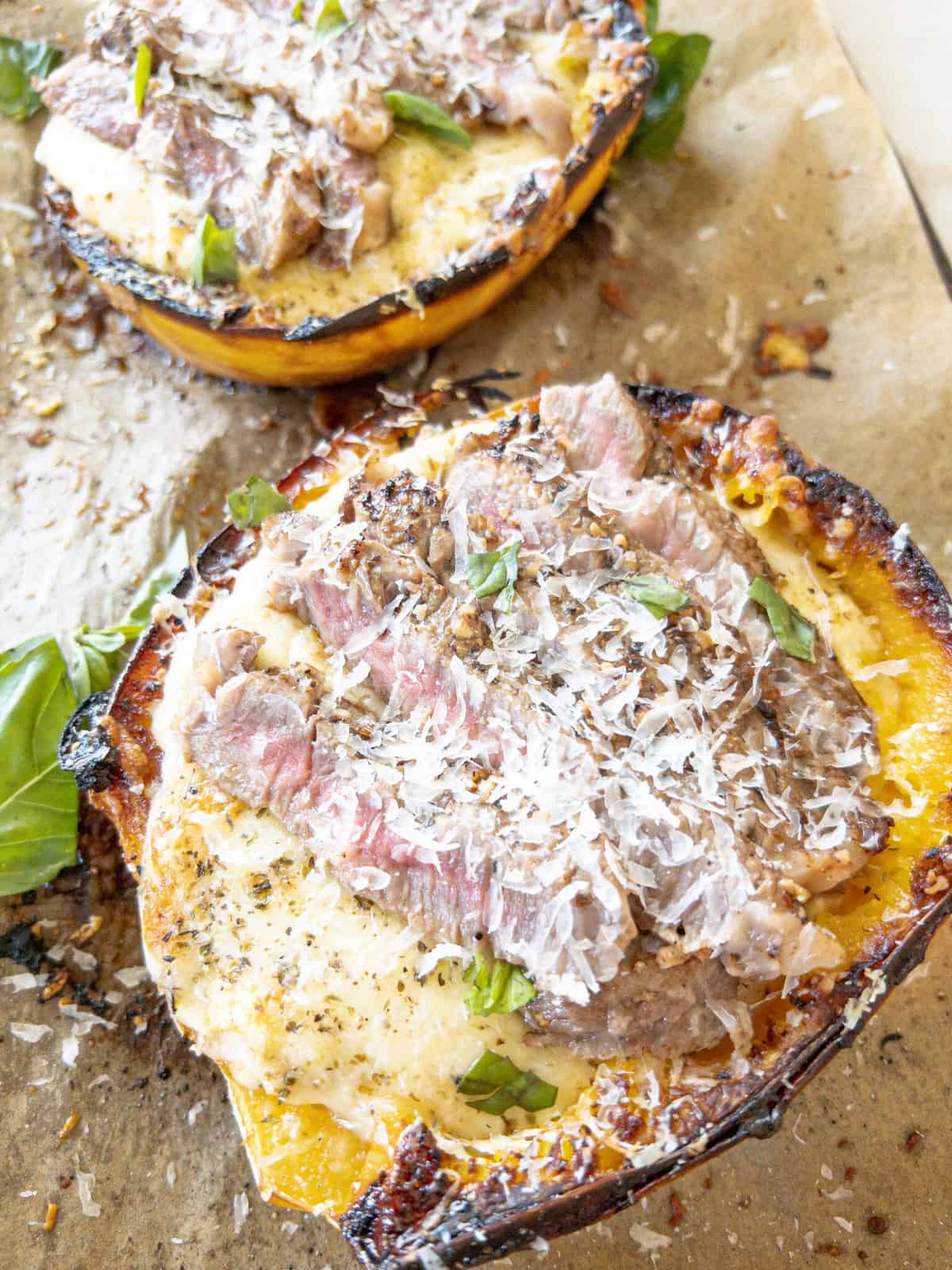 Two sliced spaghetti squashes, baked and filled with alfredo, steak and more cheese. Basil is on the side for garnish.