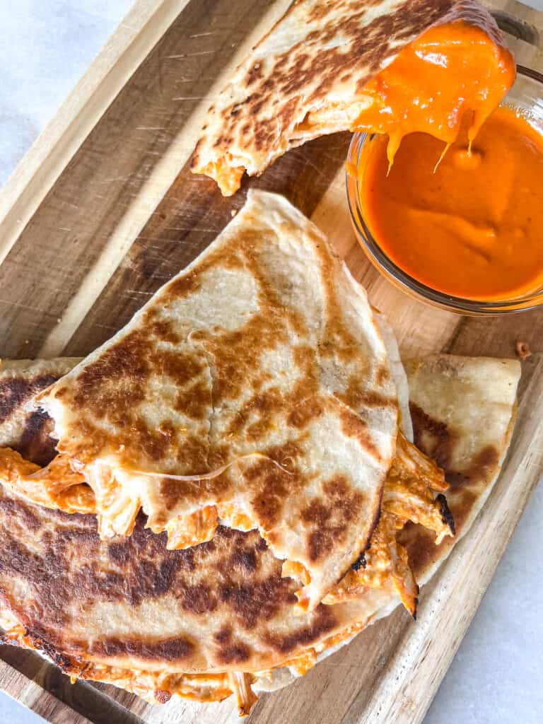 A platter of sliced quesadillas with a side of buffalo sauce.