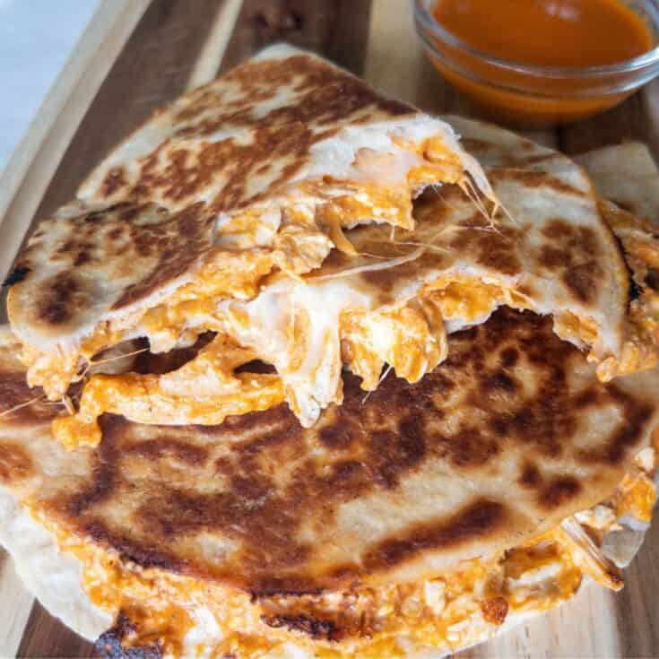 buffalo chicken quesadillas cut open on a plate with a side of hot sauce in a bowl