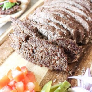 overhead view of gyro meat with tomatoes and pickles on a cutting board
