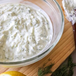 close up of tzatziki sauce in a glass bowl with a spoon beside it
