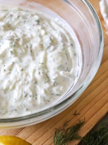 close up of tzatziki sauce in a glass bowl with a spoon beside it