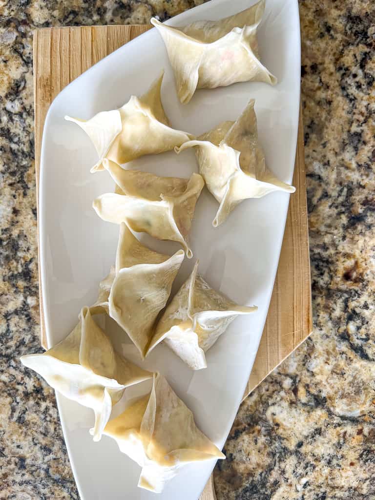 crab rangoon wrapped and sealed sitting on a plate to be air fried