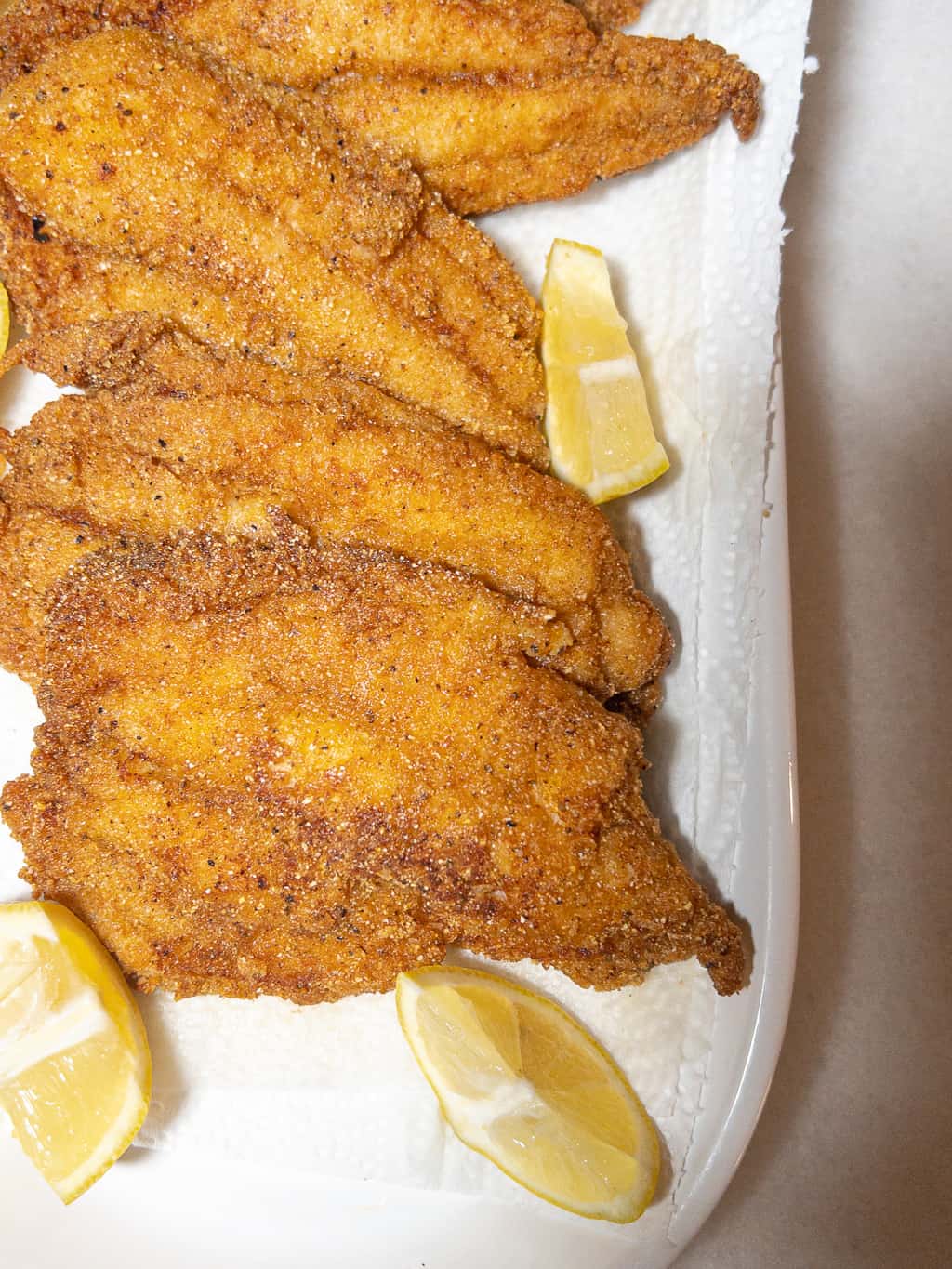 fried catfish filets on a platter with lemon wedges as a garnish