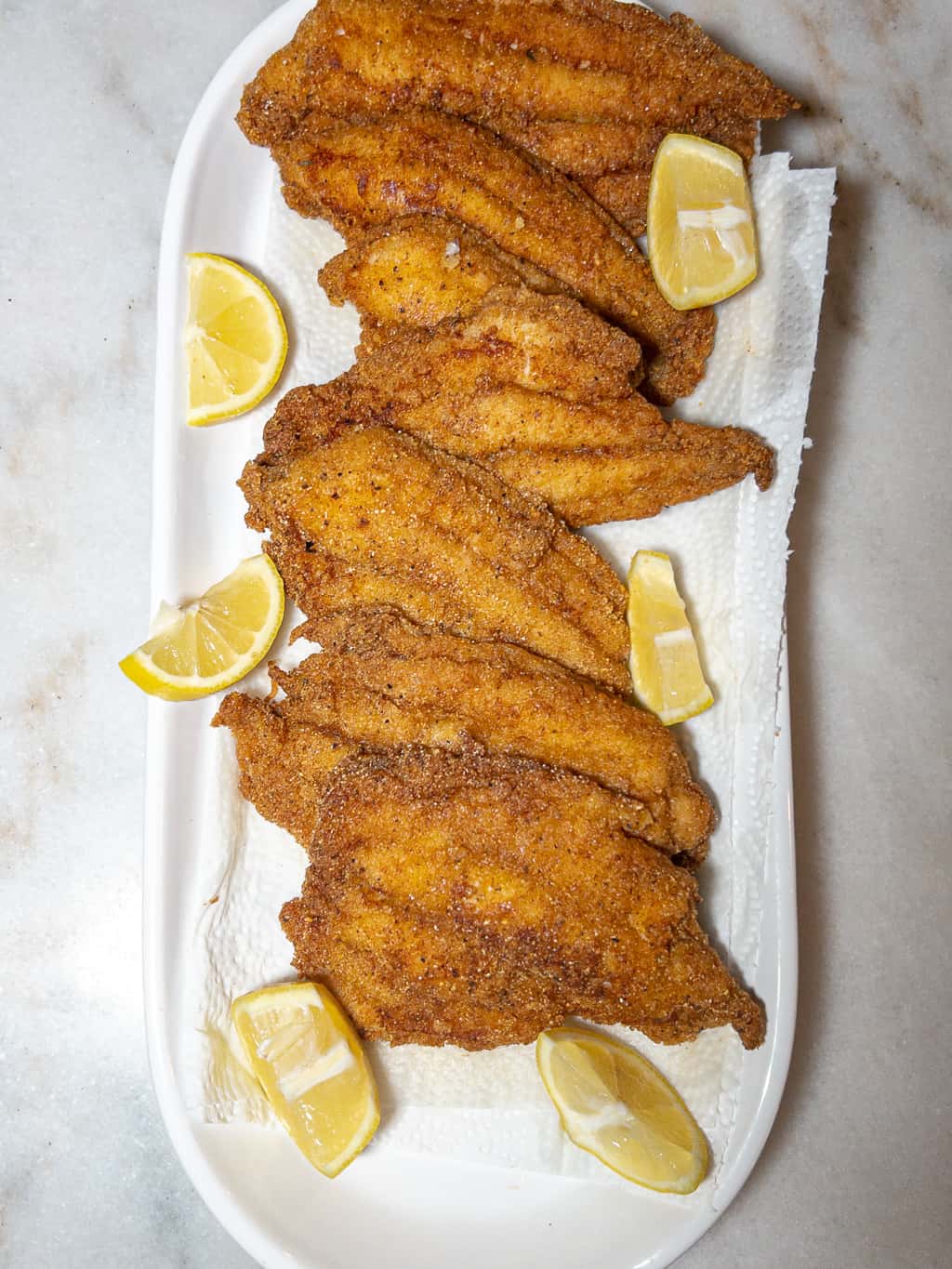 fried catfish filets on a platter with lemon wedges as a garnish
