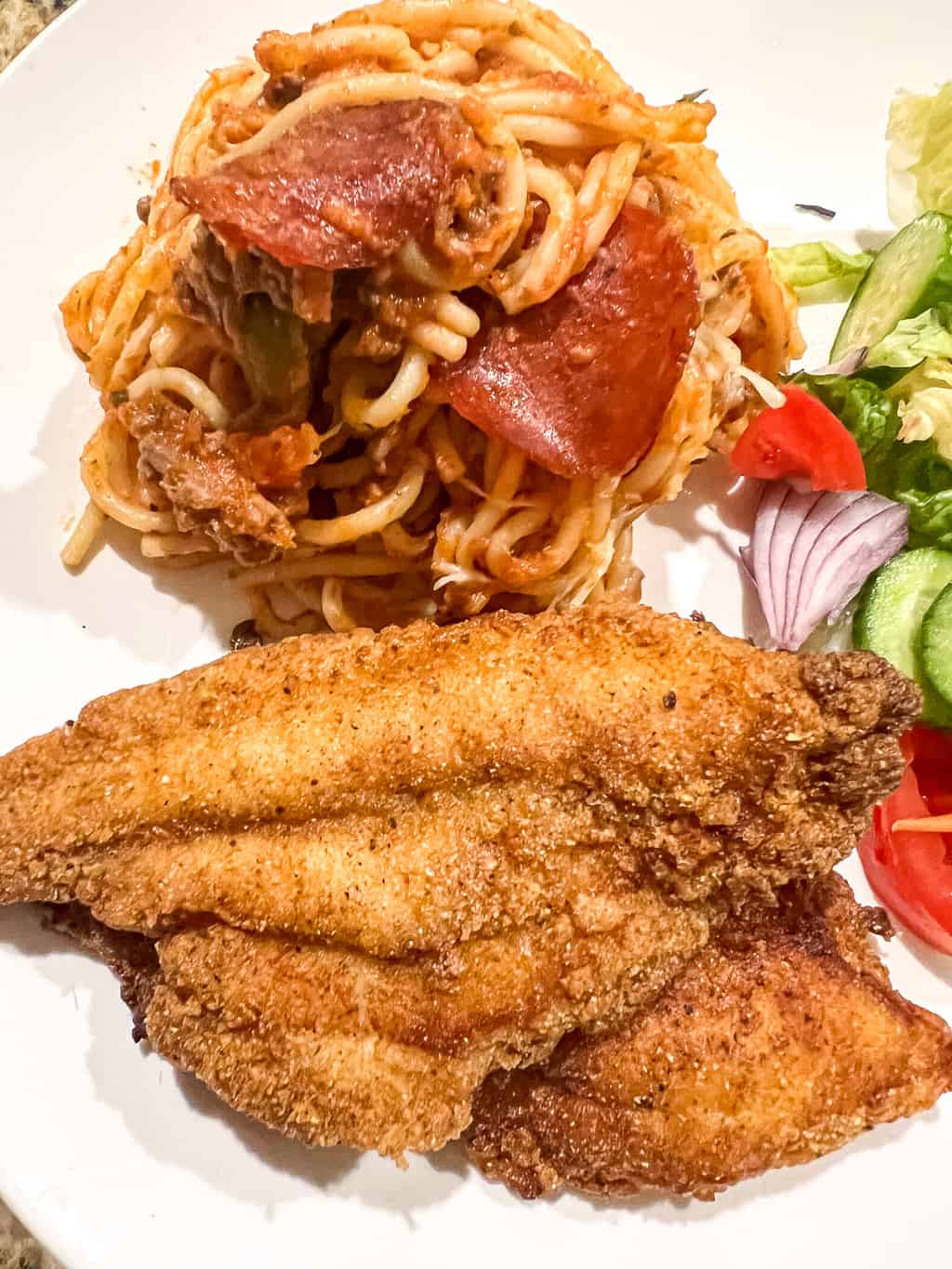 fried catfish on a plate with spaghetti and a salad