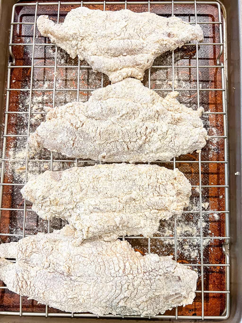 breaded catfish sitting on a cooling rack before frying