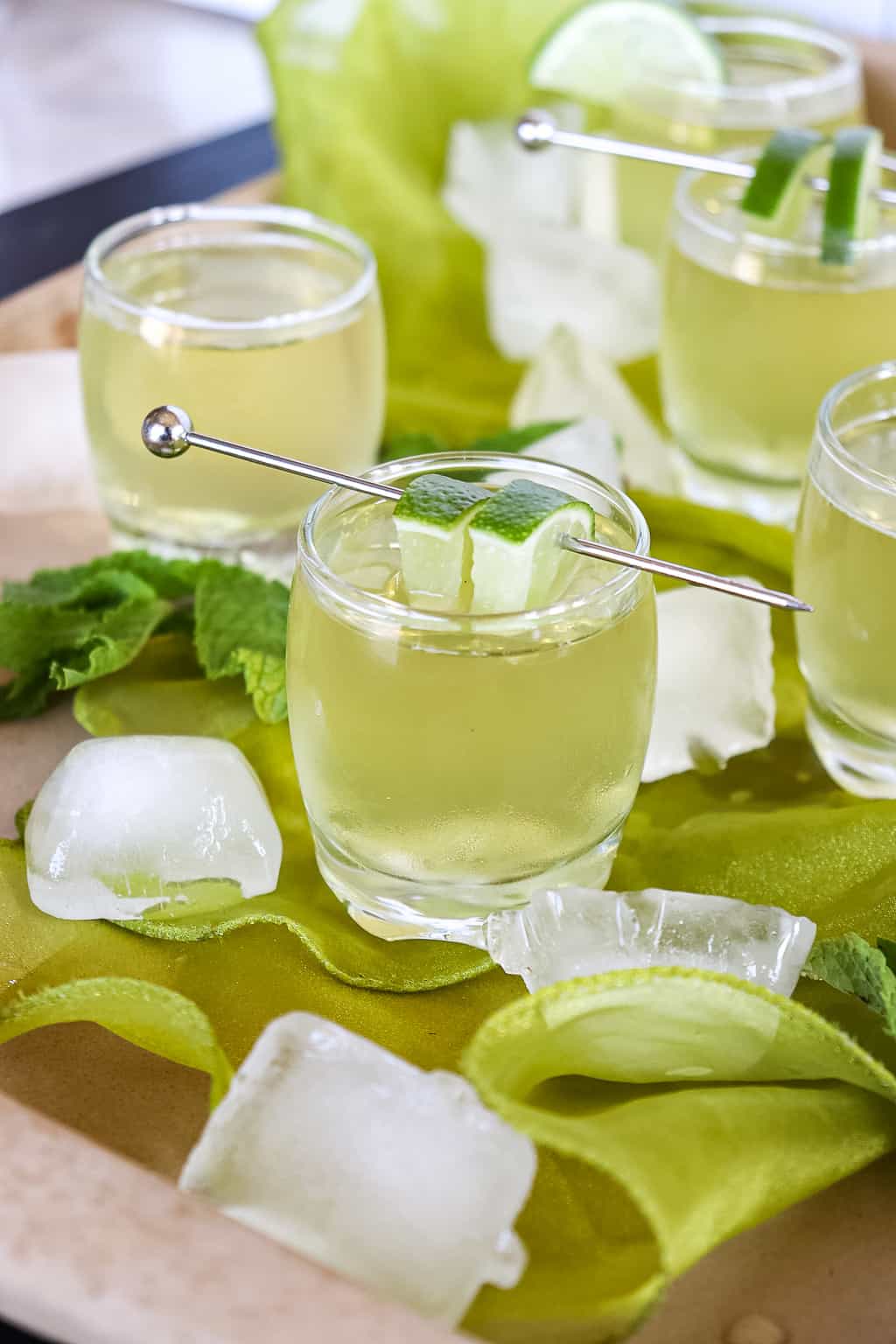 shots on a table with ice cubes around them and a lime wedge on the rim of the shot glass