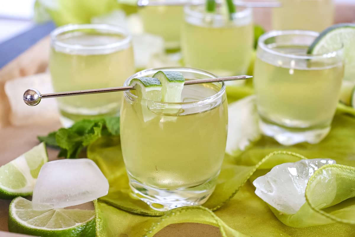 green tea shots on a table with ice cubes around them and a lime wedge on the rim of the shot glass