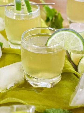 green tea shots on a table with ice cubes around them and a lime wedge on the rim of the shot glass