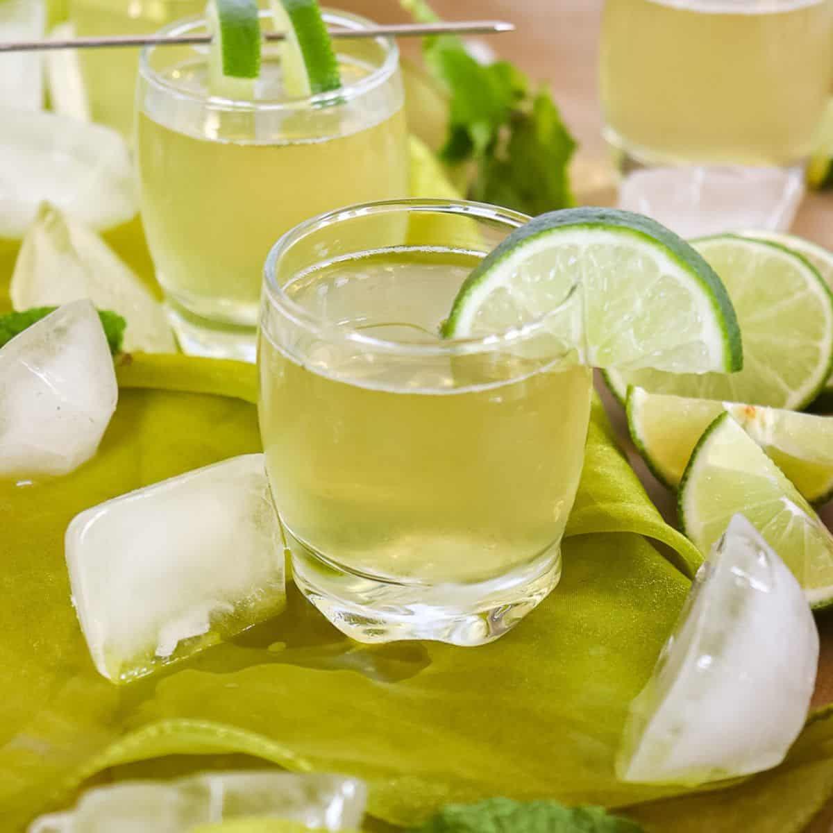 green tea shots on a table with ice cubes around them and a lime wedge on the rim of the shot glass