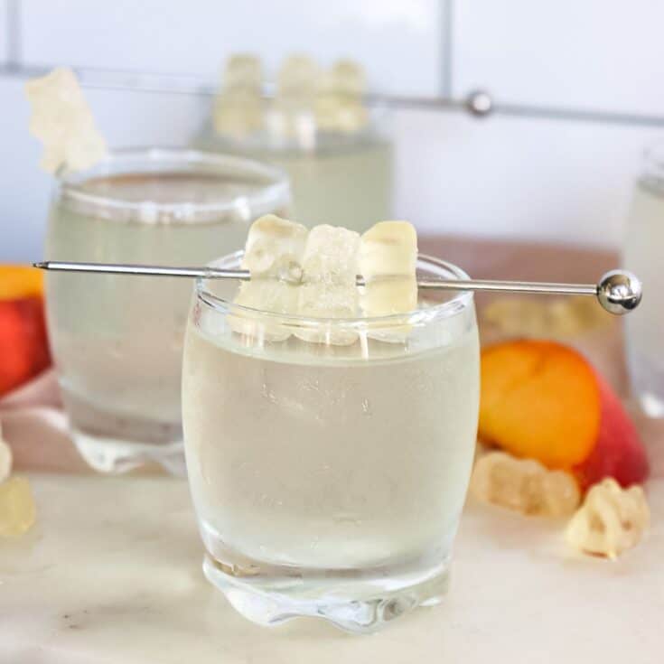 white gummy bear shot poured into a shot glass with white gummy bears on a stir stick for garnishment