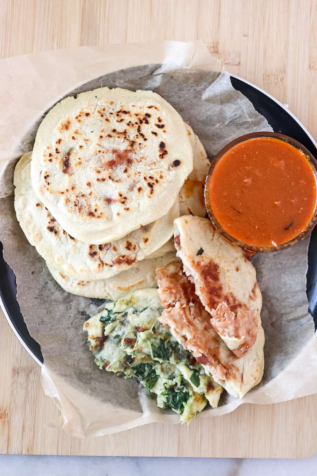 spinach and cheese and bean and cheese pupusas on a plate with salsa roja in a bowl next to it