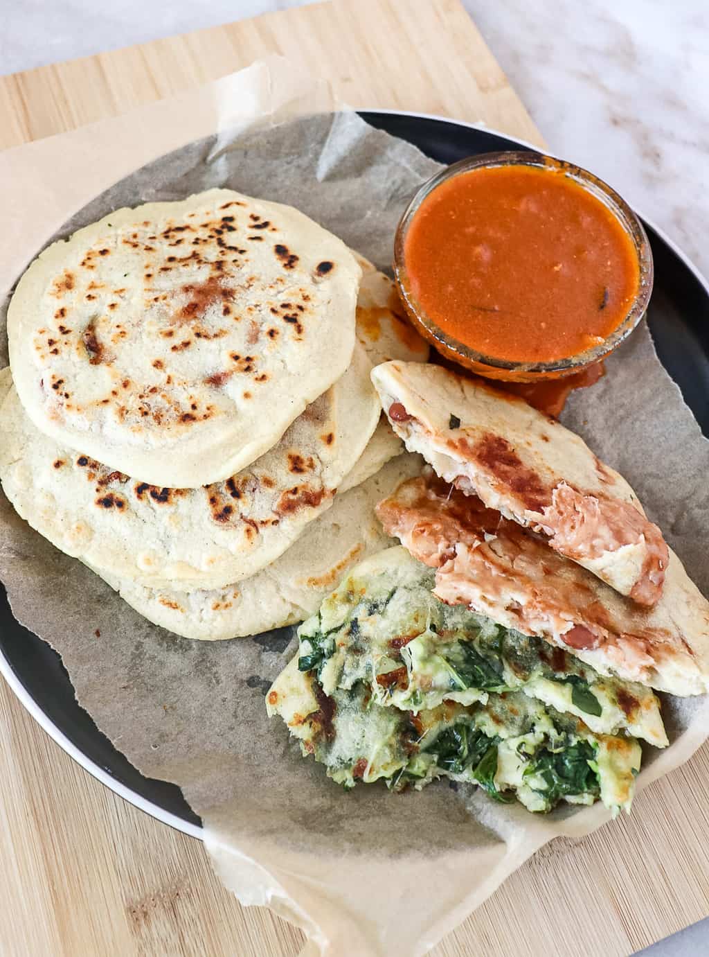 spinach and cheese and bean and cheese pupusas on a plate with salsa roja in a bowl next to it