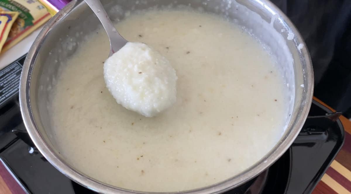 spoon scooping creamy grits out of a saucepan