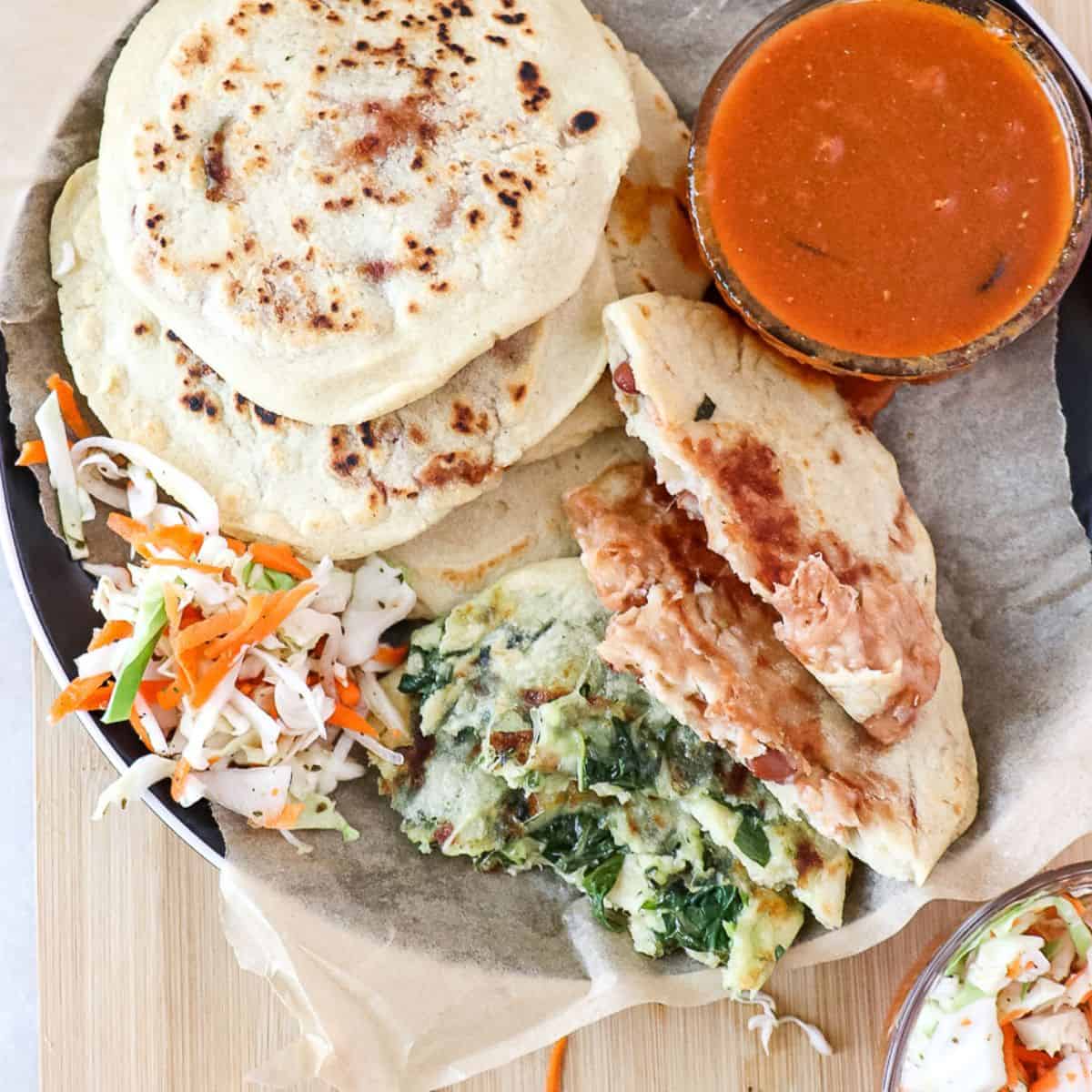 spinach and cheese and bean and cheese pupusas on a plate with salsa roja in a bowl next to it