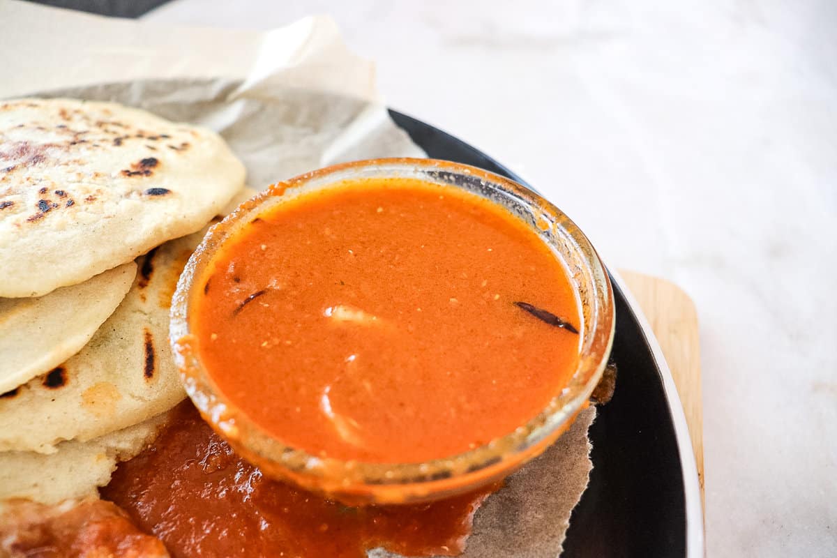 salsa roja in a small bowl on a plate next to pupusas