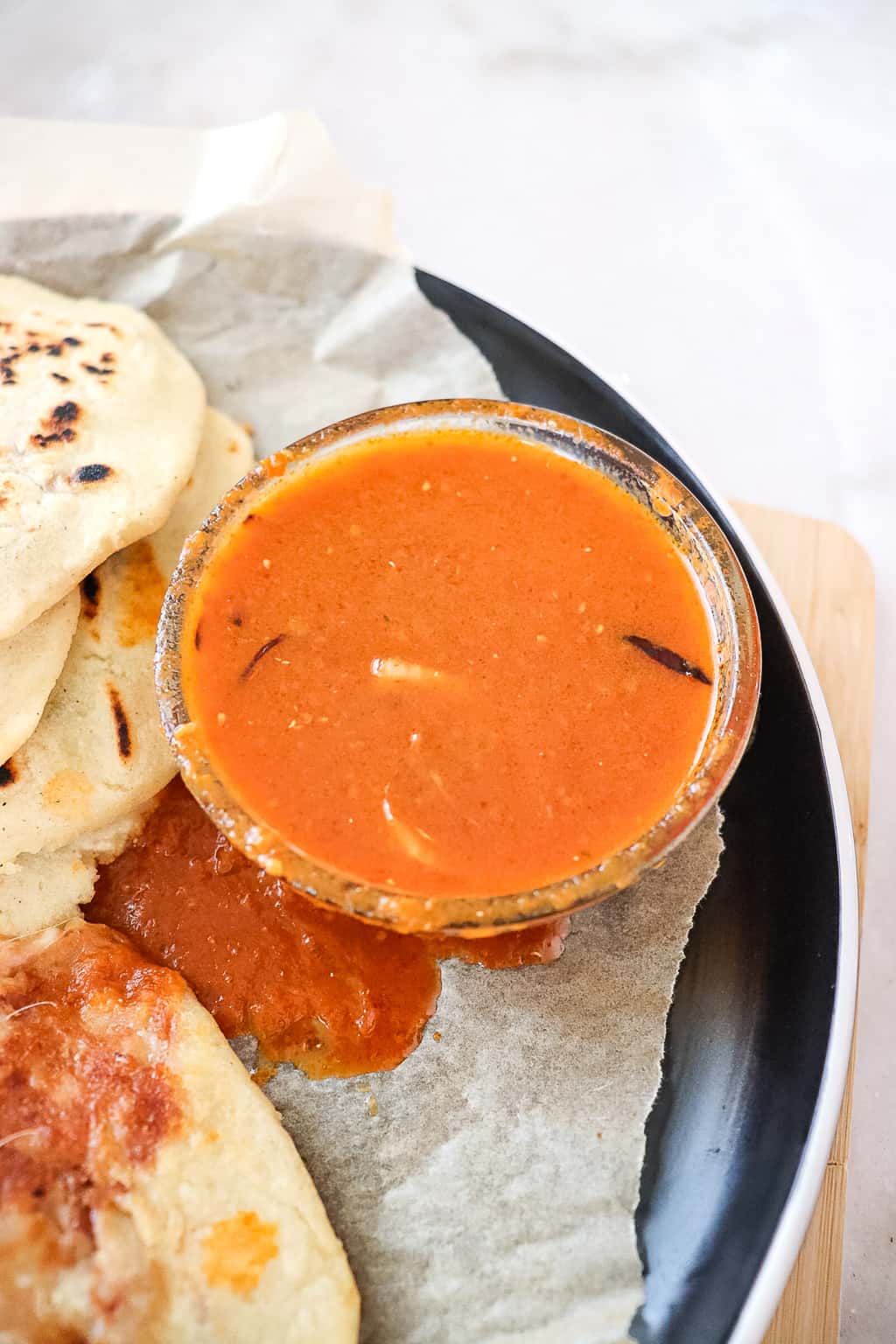 salsa roja in a small bowl on a plate next to pupusas