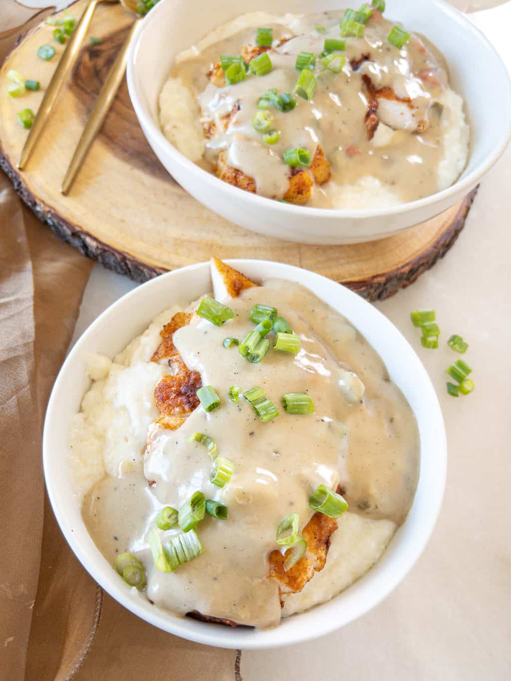 smothered chicken over grits in a bowl with green onions sprinkled on top