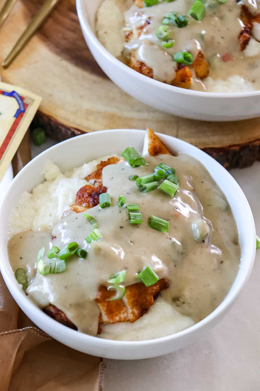 smothered chicken over grits in a bowl with green onions sprinkled on top