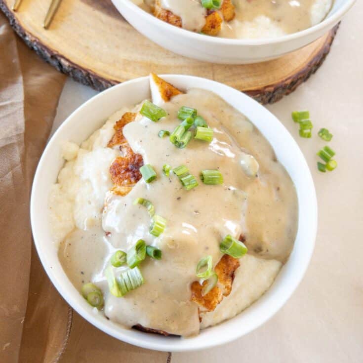 smothered chicken over grits in a bowl with green onions sprinkled on top