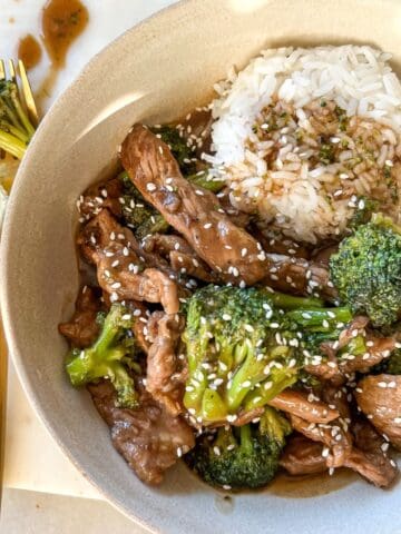 beef and broccoli in a white bowl with a side of jasmine rice