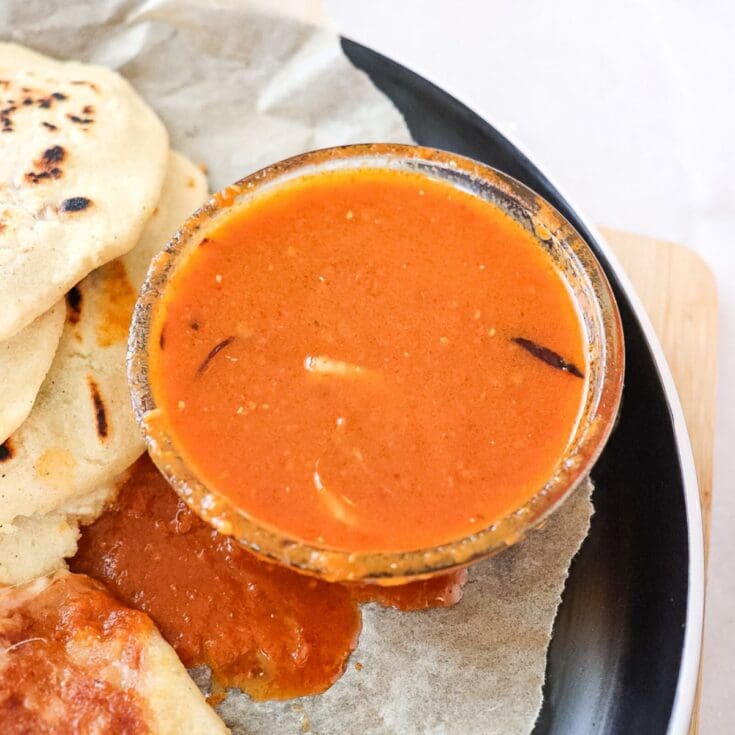 salsa roja in a small bowl on a plate next to pupusas