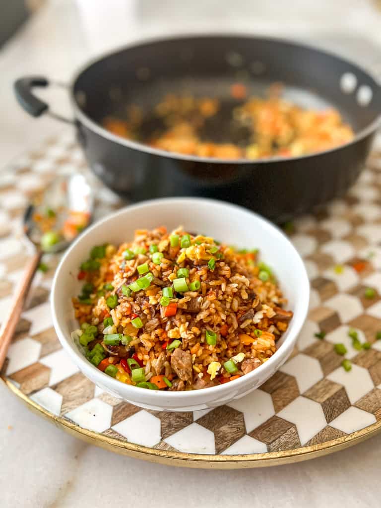 A bowl of beef fried rice with a nearly empty pot in the background