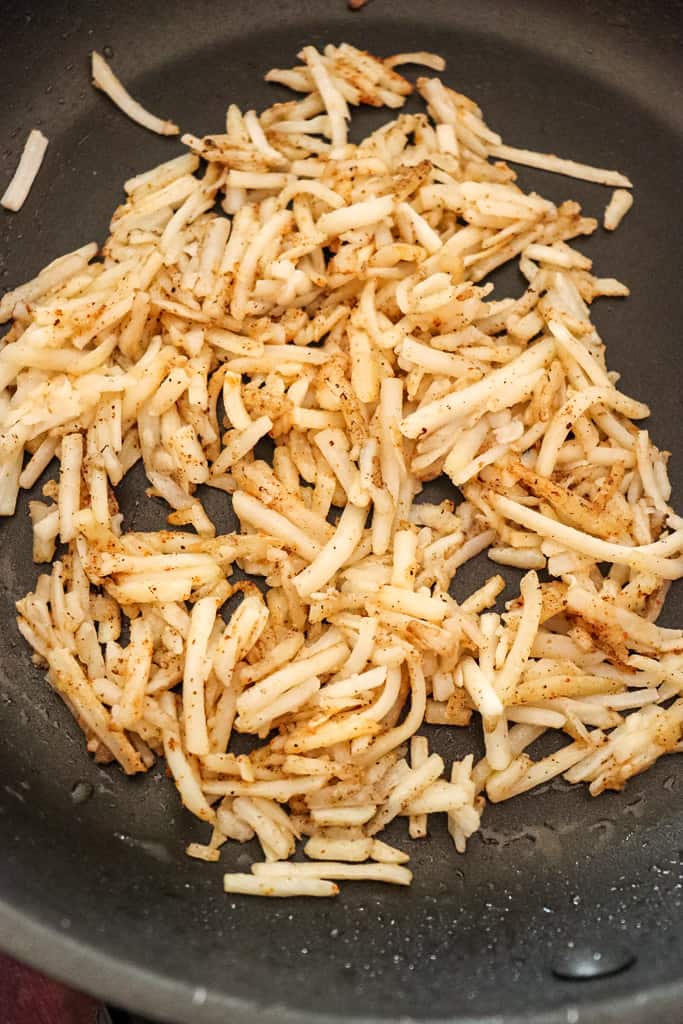 hash browns cooking in a skillet to make breakfast bowls