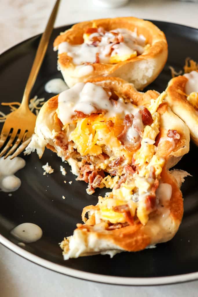 biscuit bowls with hash browns eggs and bacon on a plate with a gold fork next to it