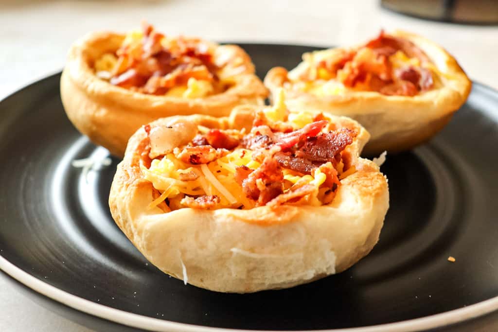 close up view of breakfast bowl with eggs bacon and cheese on a black plate