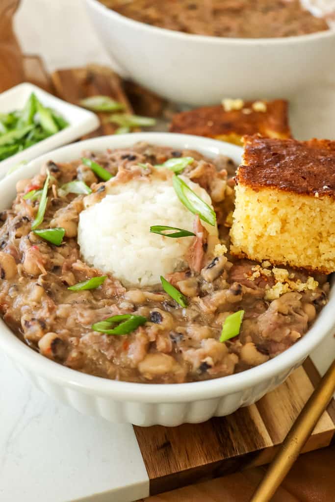 a bowl of black eyed peas topped with a scoop of white rice and a side of cornbread