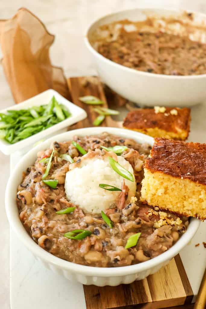 a bowl of black eyed peas topped with a scoop of white rice and a side of cornbread