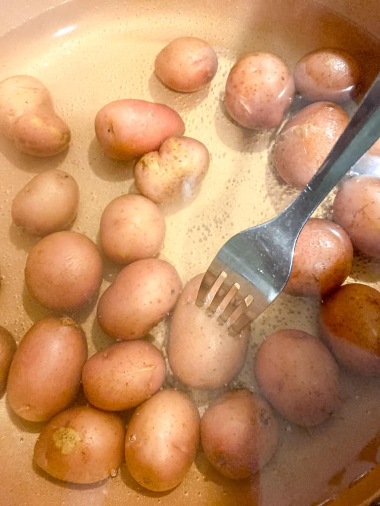 a pot full of red potatoes submerged in water with a fork inserted into one