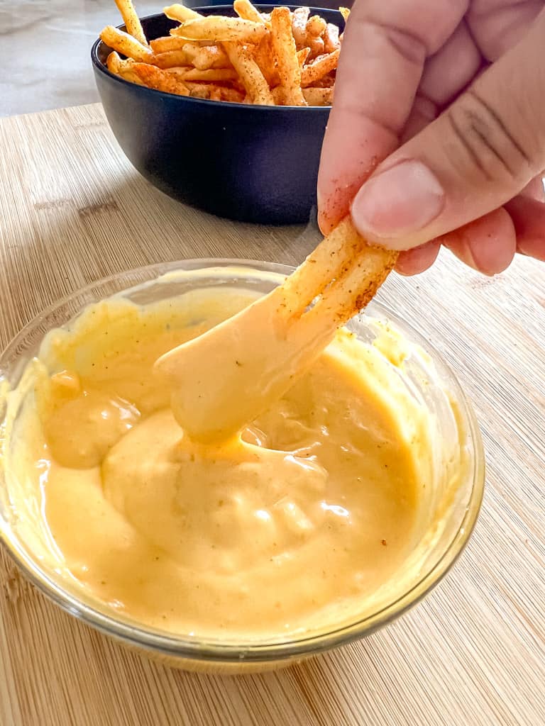 seasoned fries being dipped into cheese