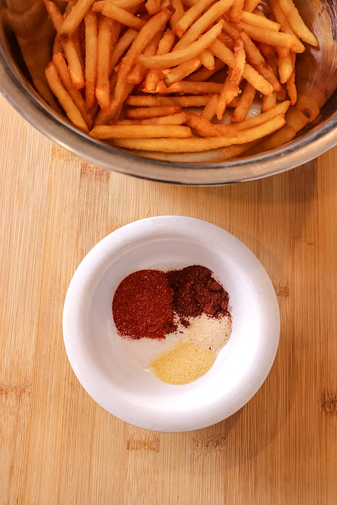overhead view of a small bowl of fry seasoning beside a larger bowl of fries