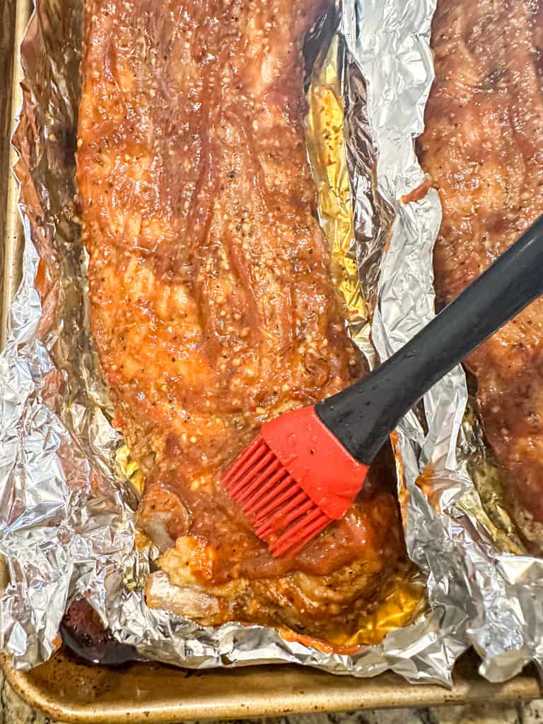 cooked ribs being coated with sauce