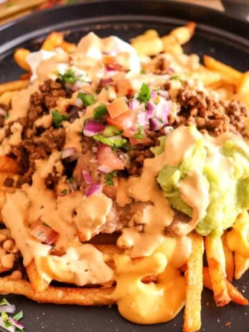 plated fries topped with cheese, ground beef, and guacamole