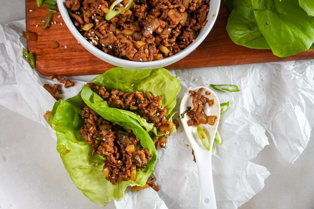 overhead view of a bowl of seasoned ground chicken and two chicken lettuce wraps