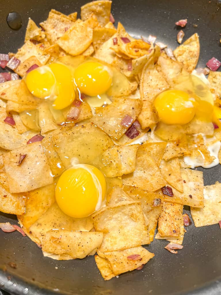 fried tortilla chips combined with raw eggs in skillet