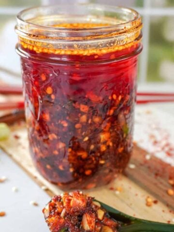 mason jar full of chili oil with a spoon full of chili flakes in front of it