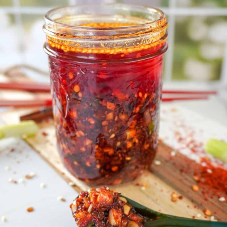 mason jar full of chili oil with a spoon full of chili flakes in front of it