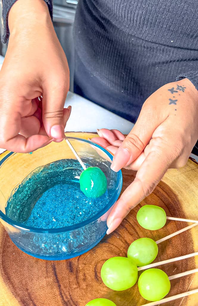 a single grape being dipped into melted blue raspberry mixture