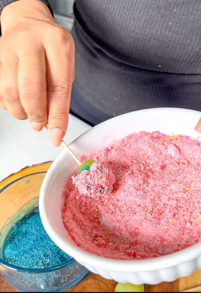 a single candy grape being rolled and coated in crushed candy