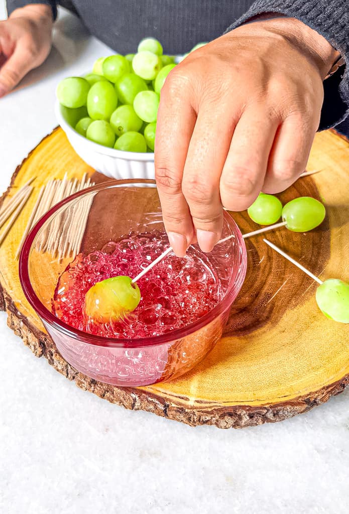 a single grape being dipped into melted watermelonmixture